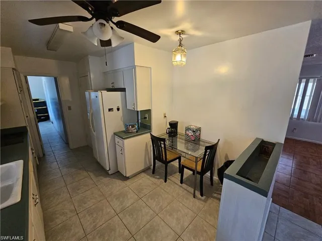 Kitchen area featuring tile flooring, ceiling-mounted fan with integrated lighting, solid-surfaced countertops, and a decorative hanging pendant light