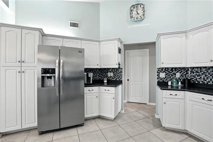 Kitchen with stainless steel refrigerator with ice dispenser, dark countertops, a towering ceiling, light tile patterned floors, and white cabinetry