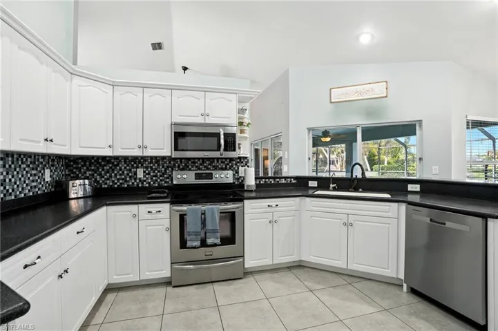 Kitchen with appliances with stainless steel finishes, lofted ceiling, tasteful backsplash, light tile patterned flooring, and white cabinetry