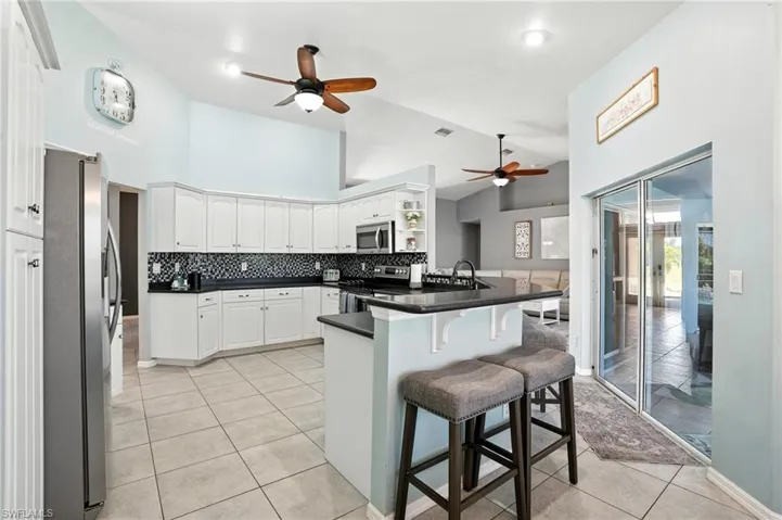 Kitchen with high vaulted ceiling, a ceiling fan, a kitchen breakfast bar, appliances with stainless steel finishes, and a peninsula