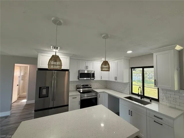 Kitchen with a textured ceiling, a sink, decorative backsplash, appliances with stainless steel finishes, and dark wood-style floors