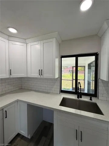 Kitchen with a sink, light stone counters, dark wood-type flooring, white cabinetry, and decorative backsplash