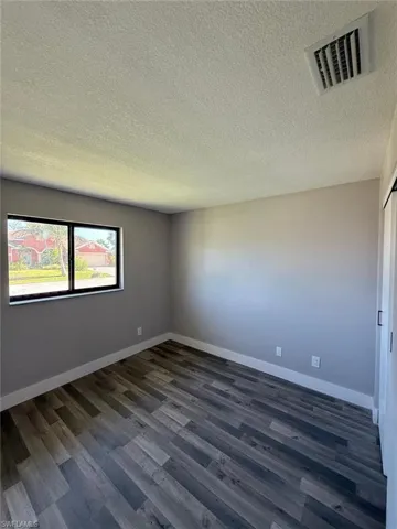 Spare room featuring baseboards, dark wood finished floors, visible vents, and a textured ceiling