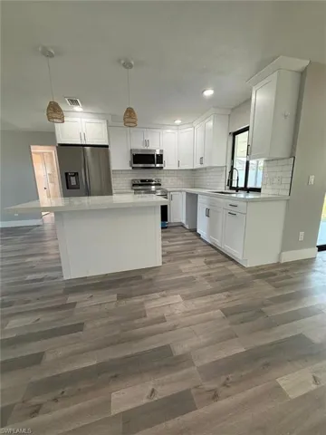 Kitchen featuring wood finished floors, a sink, white cabinets, backsplash, and appliances with stainless steel finishes
