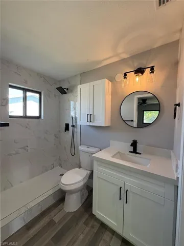 Full bath with toilet, a marble finish shower, wood finished floors, a textured ceiling, and vanity