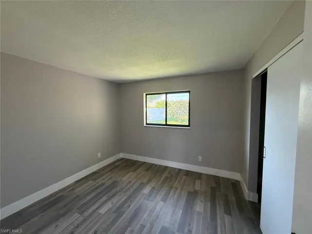 Unfurnished bedroom featuring dark wood-style flooring, a textured ceiling, baseboards, and a closet