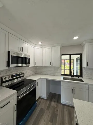 Kitchen featuring dark wood-style flooring, stainless steel appliances, white cabinets, and a sink