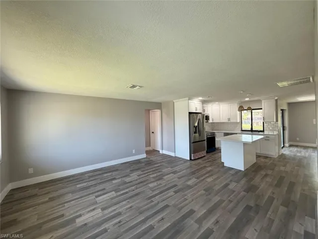 Kitchen featuring stainless steel refrigerator with ice dispenser, dark wood-type flooring, backsplash, open floor plan, and baseboards
