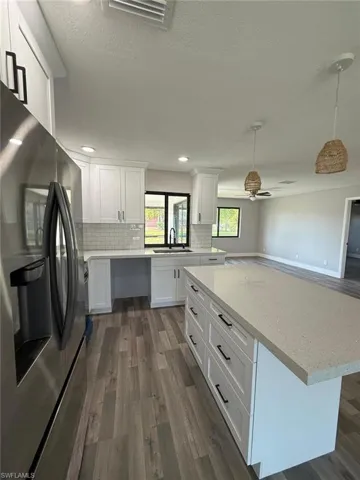Kitchen featuring stainless steel fridge, visible vents, dark wood-style floors, and white cabinets
