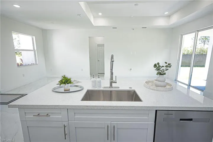 Kitchen with light stone counters, a sink, plenty of natural light, and dishwasher