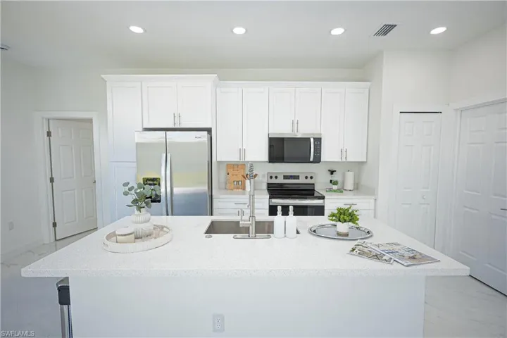 Kitchen featuring marble finish floor, a kitchen island with sink, recessed lighting, white cabinetry, and appliances with stainless steel finishes