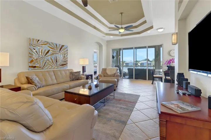 Tiled living room with a towering ceiling, ceiling fan, and a raised ceiling