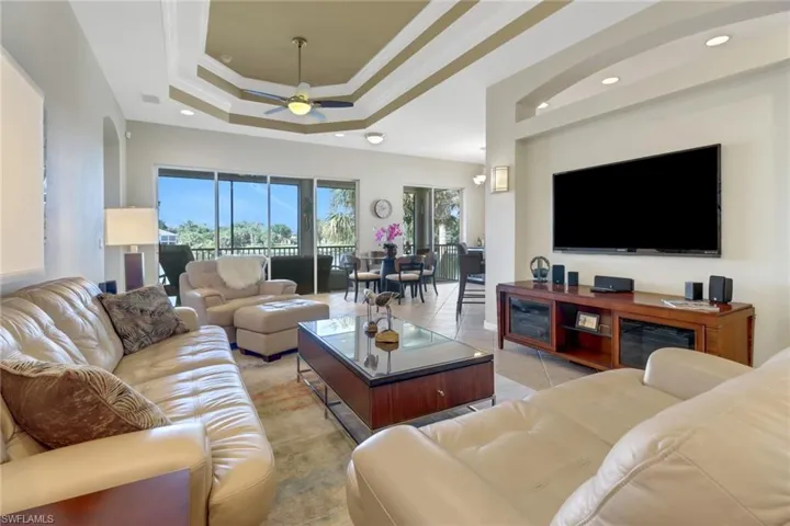 Living room featuring a raised ceiling, light tile patterned floors, ornamental molding, and ceiling fan