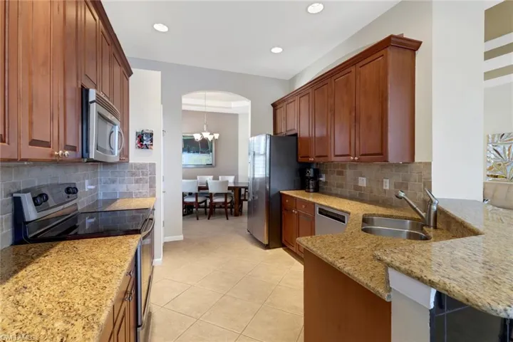 Kitchen featuring light stone counters, a chandelier, light tile patterned flooring, decorative backsplash, and stainless steel appliances