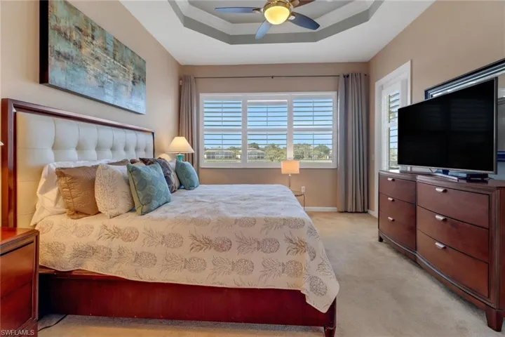 Carpeted bedroom featuring ceiling fan, a raised ceiling, and crown molding