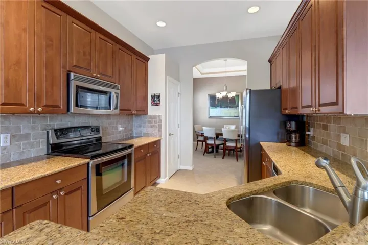 Kitchen featuring appliances with stainless steel finishes, tasteful backsplash, light stone countertops, sink, and a notable chandelier
