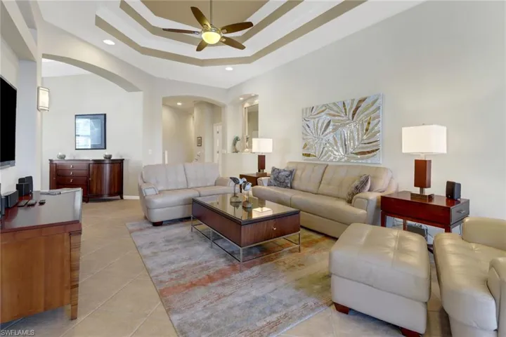 Living room with ceiling fan, a raised ceiling, and light tile patterned floors