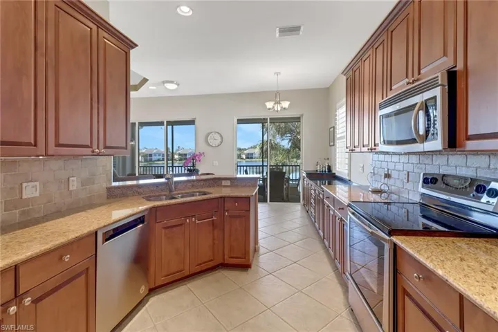 Kitchen with light stone counters, sink, decorative light fixtures, stainless steel appliances, and a notable chandelier