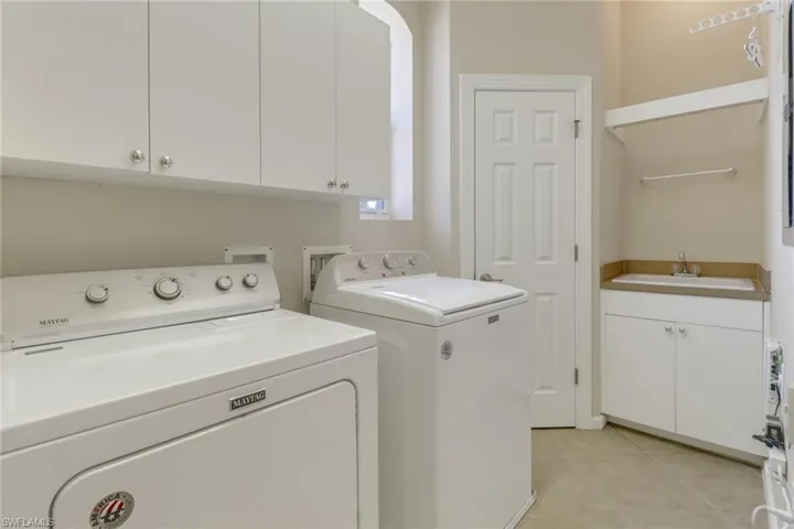 Laundry room featuring washer and clothes dryer, light tile patterned flooring, sink, and cabinets