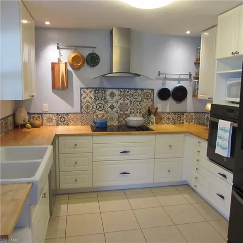 Kitchen with black appliances, butcher block counters, white cabinets, and exhaust hood