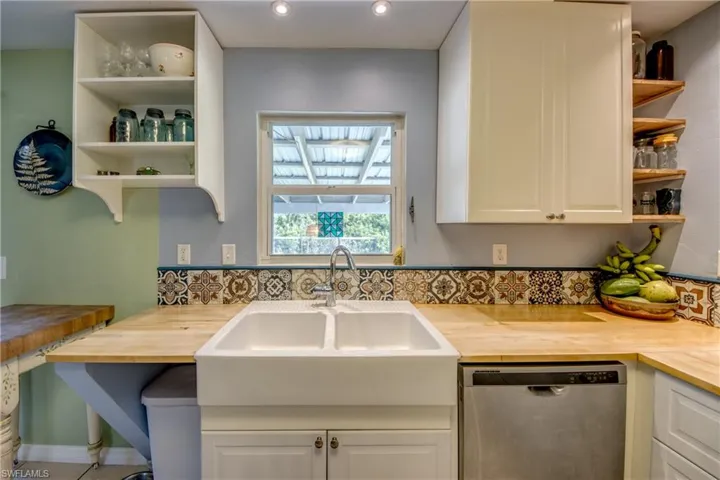 Kitchen featuring butcher block counters, sink, white cabinets, and stainless steel dishwasher
