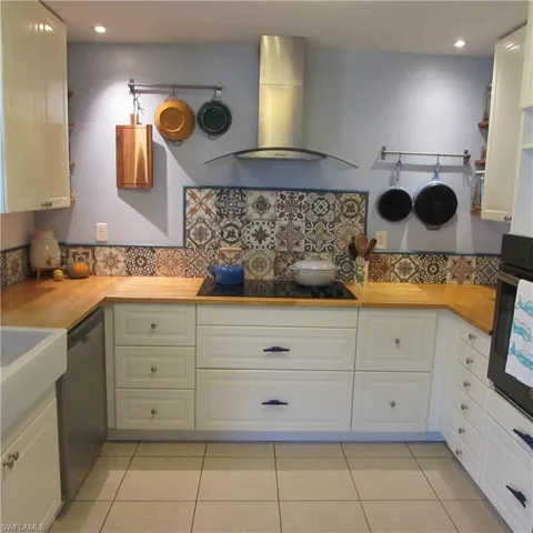 Kitchen with butcher block countertops, white cabinetry, black appliances, and exhaust hood