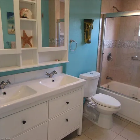 Full bathroom with vanity, backsplash, tile patterned floors, bath / shower combo with glass door, and toilet