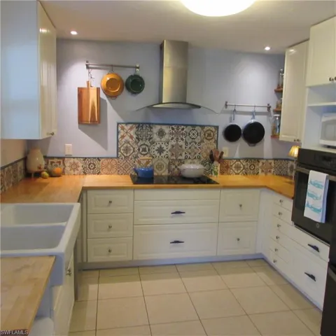 Kitchen featuring wall oven, backsplash, exhaust hood, white cabinets, and butcher block counters