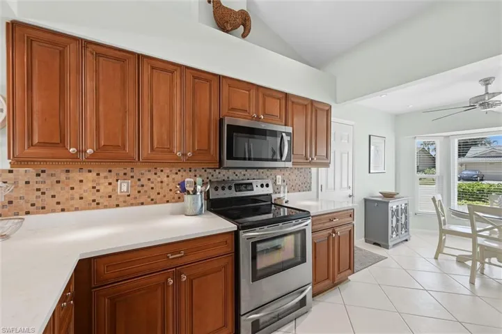 Kitchen featuring wood cabinetry, stainless steel appliances, mosaic tile backsplash, light-toned countertops, and tile flooring