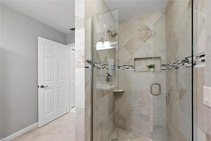 Glass-enclosed shower with tile surround, mosaic accent band, built-in niche, and corner shelf