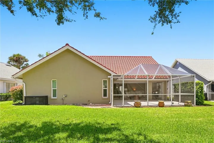 Expansive green lawn with a screened-in patio featuring a tiled roof and stucco exterior
