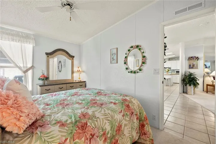 Tiled bedroom featuring connected bathroom, ceiling fan, crown molding, and a textured ceiling