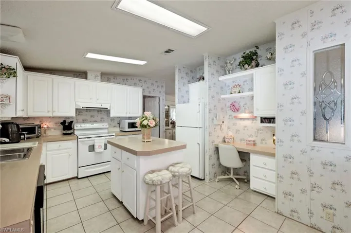 Kitchen with a center island, light tile patterned flooring, white appliances, and white cabinetry