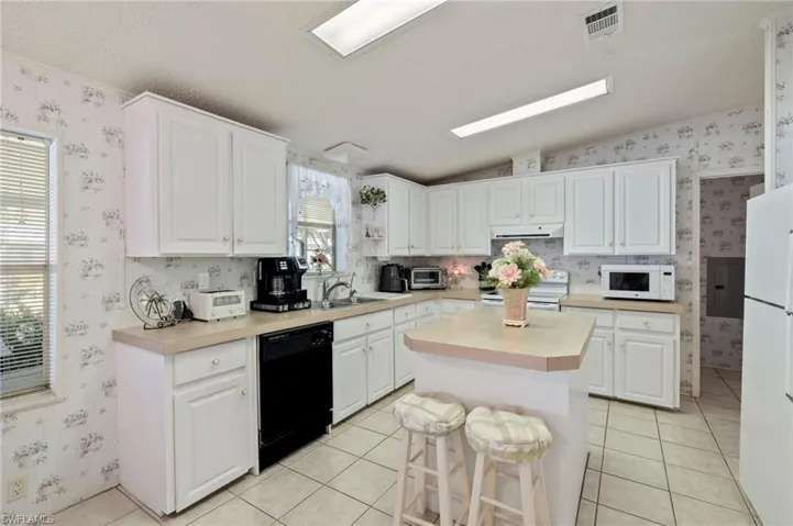 Kitchen featuring white appliances, white cabinetry, a kitchen island, and light tile patterned flooring