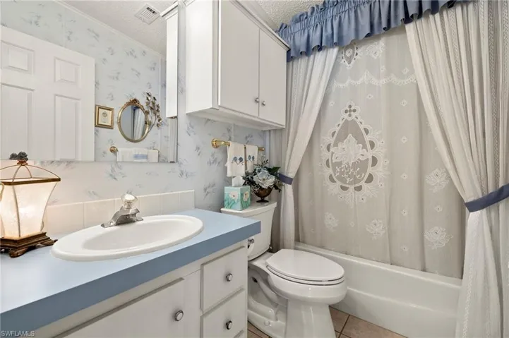 Full bathroom with tile patterned flooring, vanity, shower / bath combo with shower curtain, and a textured ceiling