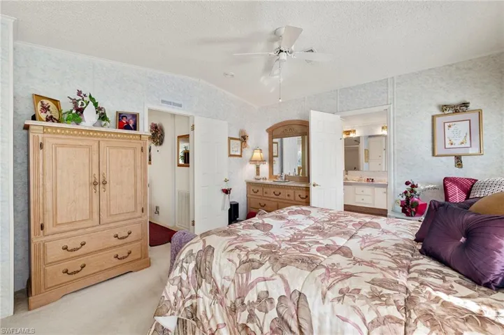 Carpeted bedroom featuring a textured ceiling, ensuite bathroom, ceiling fan, and vaulted ceiling