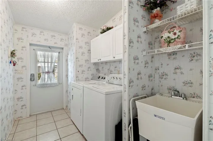 Laundry area featuring washing machine and clothes dryer, sink, cabinets, a textured ceiling, and light tile patterned floors.  Washer and dryer to remain.
