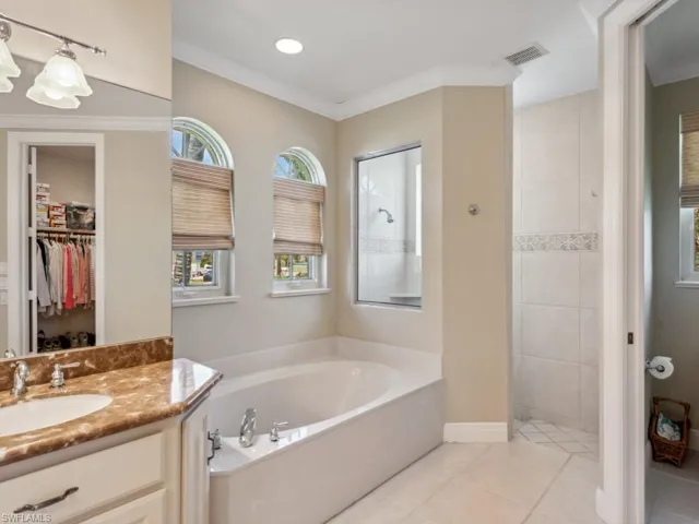 Bathroom with a bath, vanity, tile patterned flooring, a tile shower, and a spacious closet
