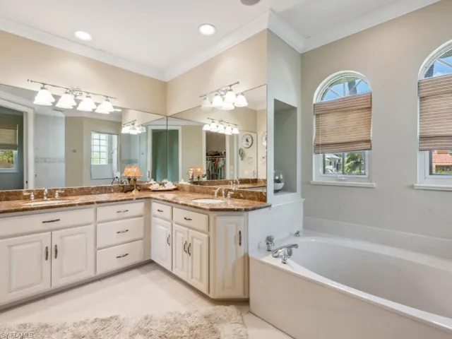 Bathroom featuring double vanity, a garden tub, crown molding, tile patterned flooring, and a chandelier