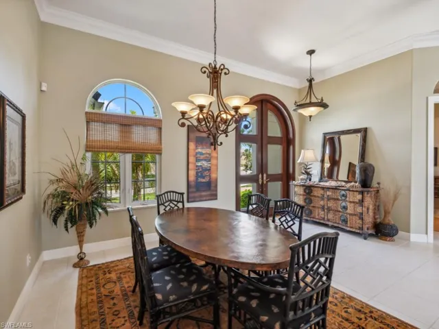 Dining area featuring light tile patterned floors, a chandelier, crown molding, arched walkways, and baseboards