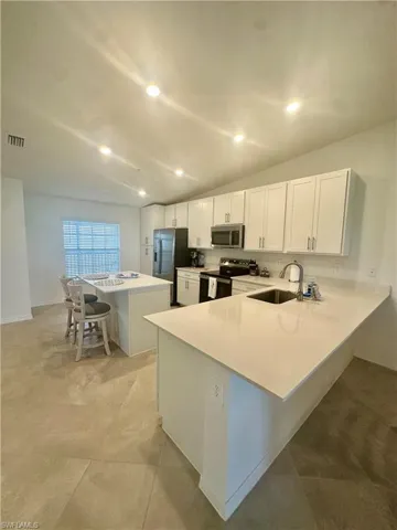 Kitchen featuring a sink, stainless steel appliances, light countertops, a breakfast bar area, and white cabinets
