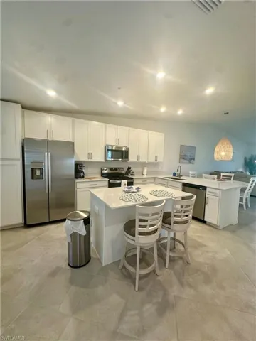 Kitchen featuring appliances with stainless steel finishes, a kitchen bar, white cabinetry, light countertops, and recessed lighting