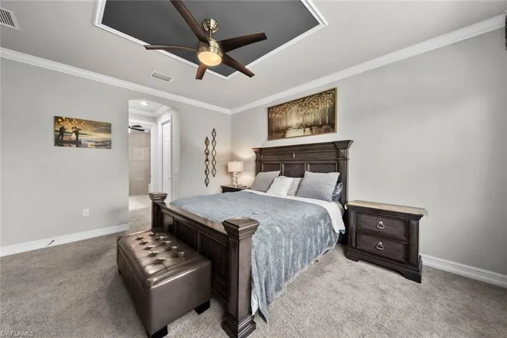 Primary bedroom with ornamental molding, light colored carpet, and ceiling fan