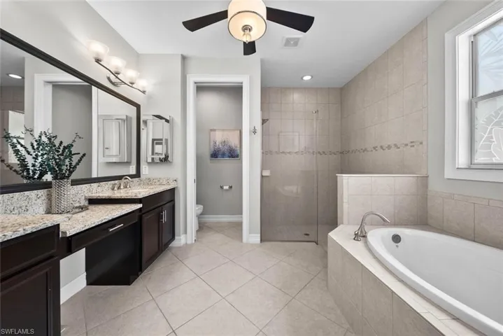 Primary bathroom suite featuring vanity, separate shower and tub, toilet, tile  and ceiling fan