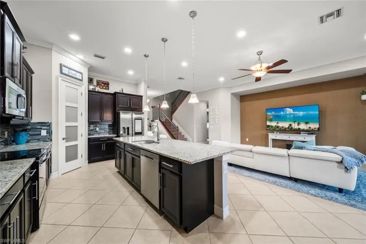 Kitchen featuring stainless steel appliances,  light stone countertops, ceiling fan, and a center island with sink