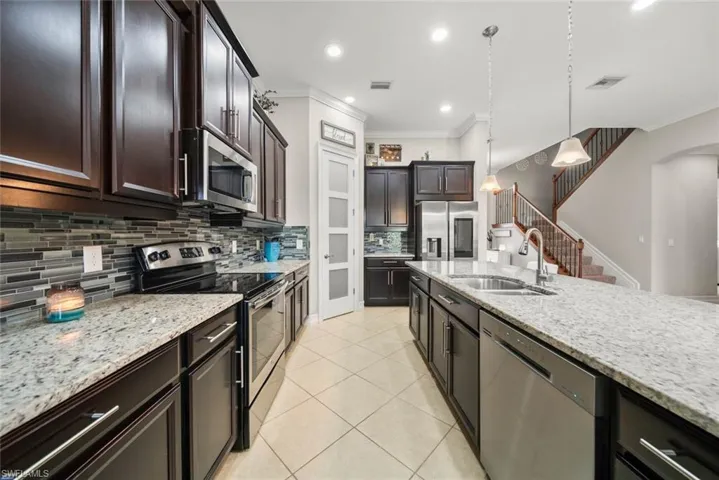 Kitchen featuring pendant lighting, backsplash, light stone counters, sink, and appliances with stainless steel finishes