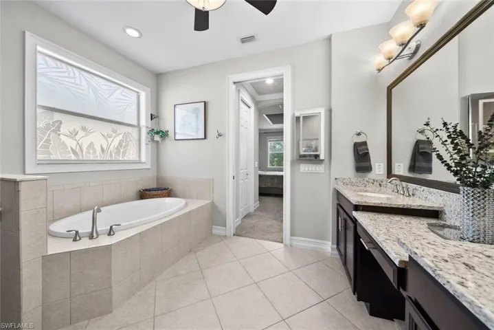 Primary Bathroom featuring vanity, ceiling fan, tiled bath, and a healthy amount of sunlight
