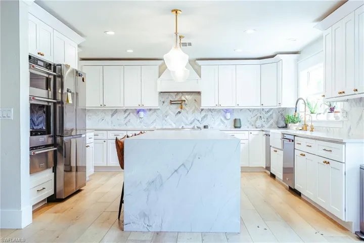 Kitchen with light wood-style floors, tasteful backsplash, a warming drawer, a center island, and appliances with stainless steel finishes