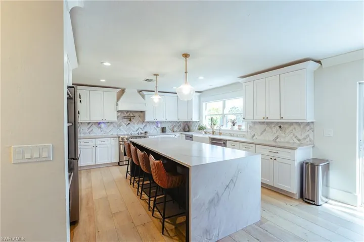 Kitchen featuring appliances with stainless steel finishes, a breakfast bar, premium range hood, and backsplash