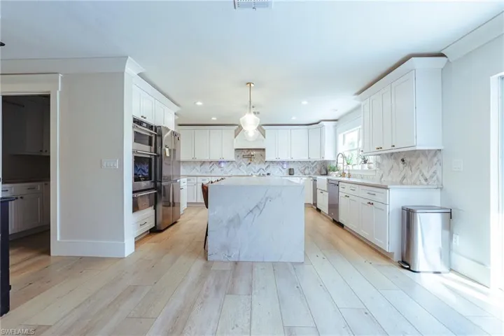 Kitchen with decorative backsplash, a warming drawer, a center island, light wood-style flooring, and appliances with stainless steel finishes
